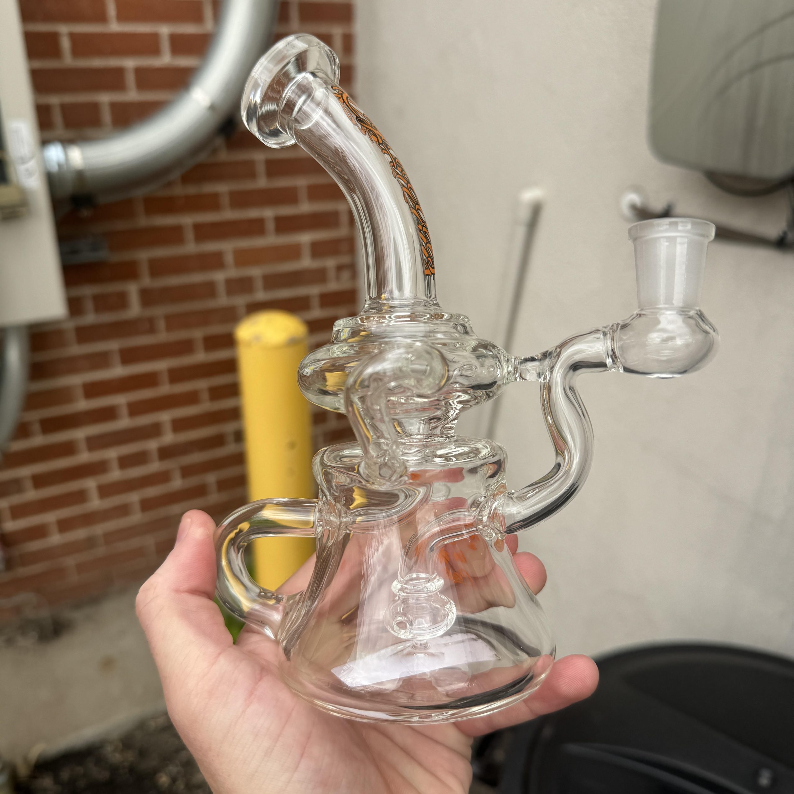 Transparent glass recycler bong in hand beside brick wall