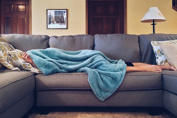 Person napping under blue fuzzy blanket on living room couch