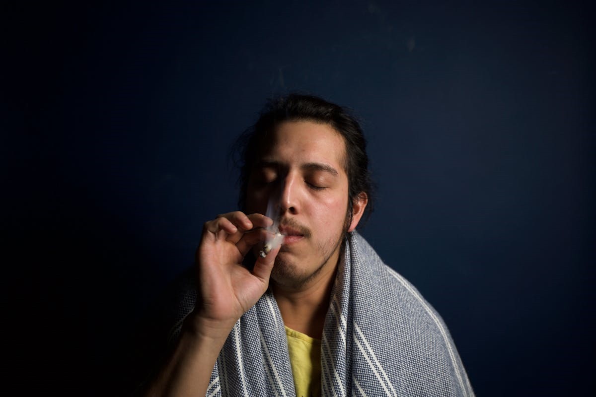 Dark-haired man smoking cannabis joint with towel draped over shoulders